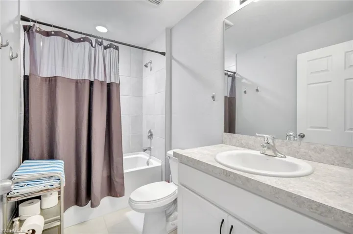 Full bath featuring shower / bath combo, vanity, light tile patterned flooring, and a textured wall