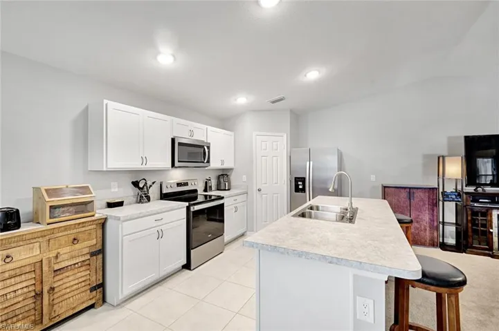 Kitchen featuring stainless steel appliances, white cabinets, light countertops, a kitchen breakfast bar, and an island with sink