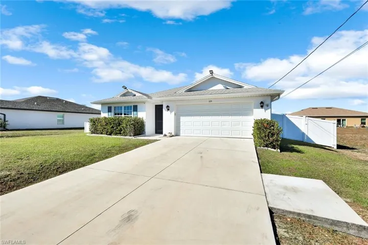 Ranch-style home featuring a front yard, stucco siding, a garage, driveway, and a gate