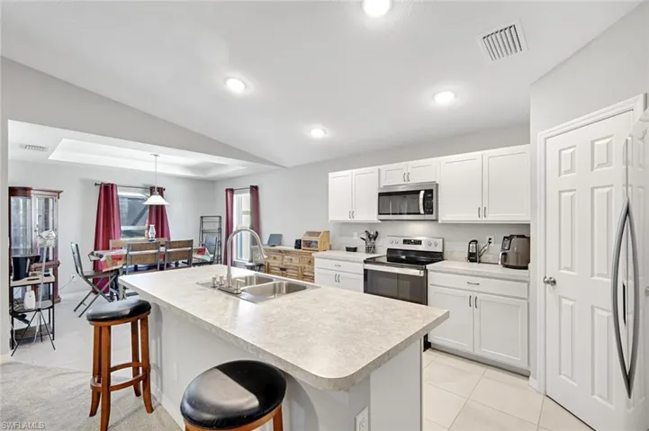 Kitchen featuring a kitchen bar, white cabinets, light tile patterned floors, vaulted ceiling, and light countertops