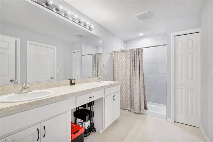 Bathroom featuring double vanity, a closet, a stall shower, and light tile patterned floors