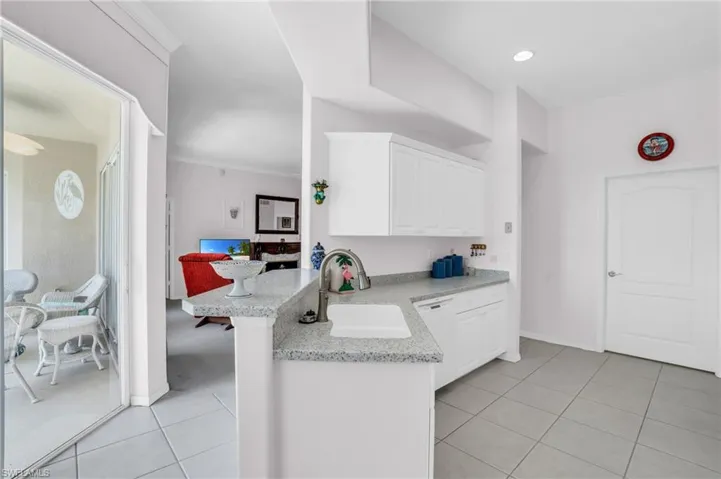 Kitchen with light tile patterned floors, kitchen peninsula, white cabinets, light stone counters, and sink