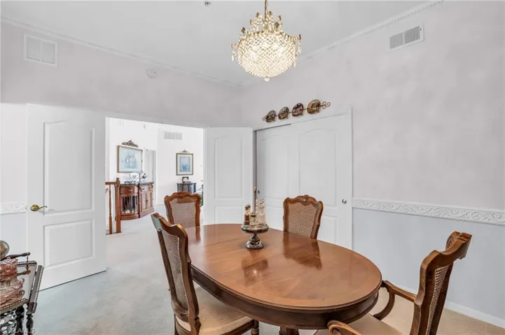 Carpeted dining room with a notable chandelier and ornamental molding