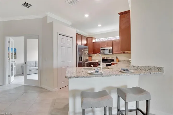 Kitchen with stainless steel appliances, sink, light tile patterned floors, light stone countertops, and crown molding