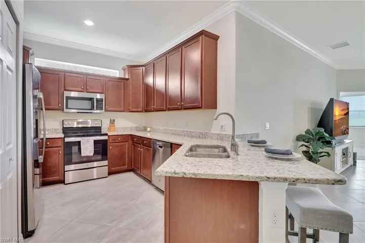 Kitchen featuring light tile patterned flooring, sink, light stone counters, and stainless steel appliances
