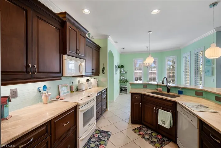 Kitchen with light tile patterned floors, decorative light fixtures, white appliances, and sink