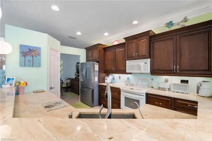 Kitchen with sink, dark brown cabinets, light tile patterned floors, and white appliances