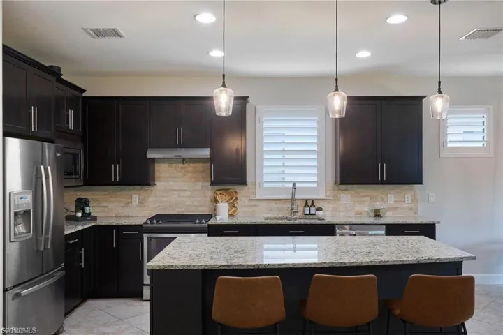 Kitchen featuring appliances with stainless steel finishes, a center island, light stone counters, decorative light fixtures, and recessed lighting