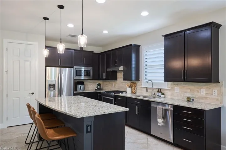 Kitchen featuring light stone counters, stainless steel appliances, pendant lighting, a kitchen bar, and decorative backsplash
