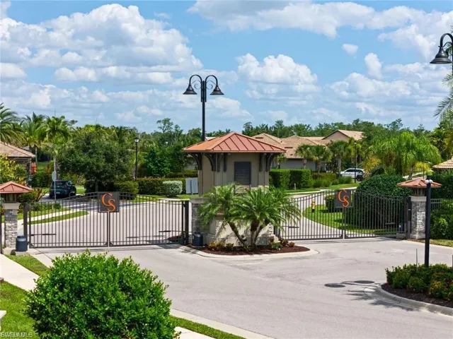 View of asphalt street with street lights, a gate, curbs, and a gated entry