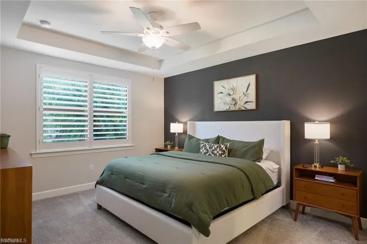 Bedroom with a raised ceiling, carpet floors, and a ceiling fan