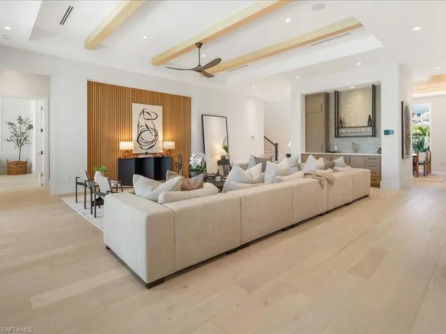 Living area featuring light wood-style flooring, beamed ceiling, stairs, a ceiling fan, and a raised ceiling