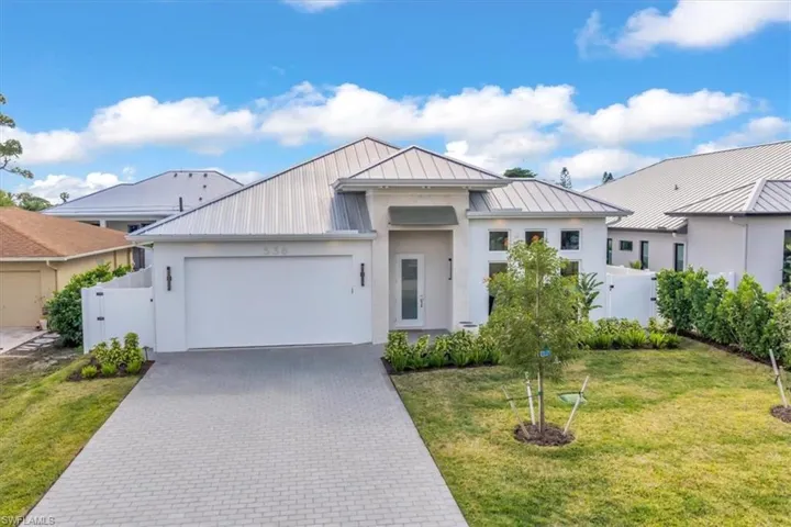View of front of home with stucco siding, decorative driveway, a metal roof, a garage, and a gate