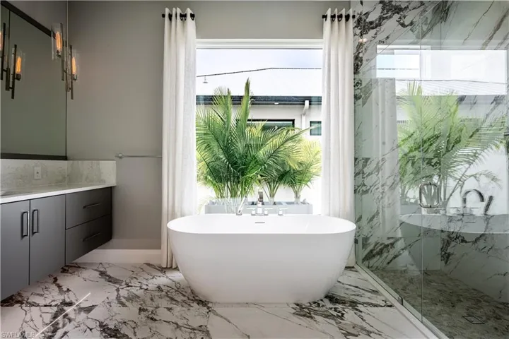 Full bath featuring light marble finish flooring, vanity, a soaking tub, and healthy amount of natural light