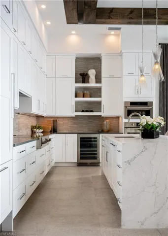 Kitchen featuring white cabinetry, light stone countertops, a chandelier, pendant lighting, and beamed ceiling