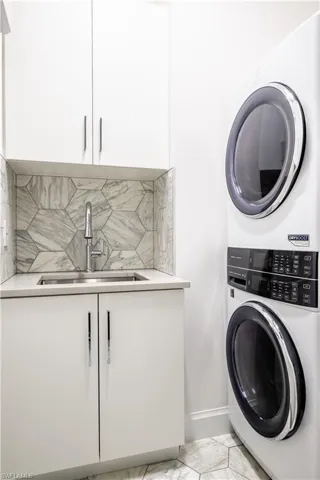Laundry room featuring cabinet space, stacked washing machine and dryer, and light marble finish flooring