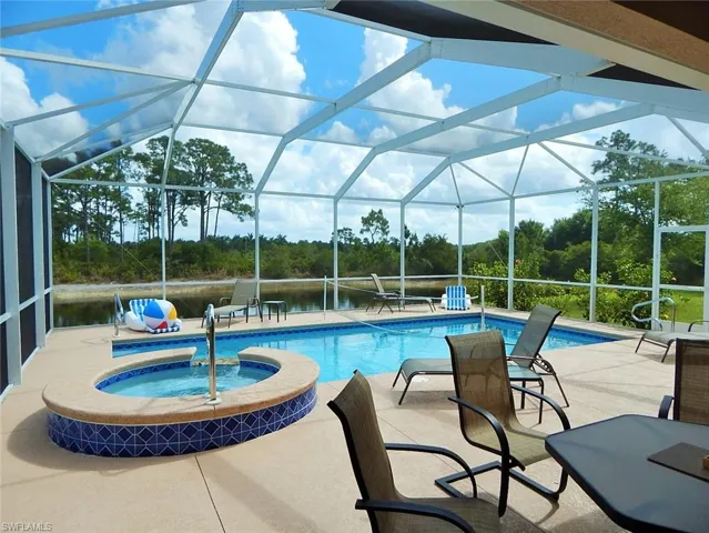 View of pool with a patio, a pool with connected hot tub, view of wooded area, and glass enclosure