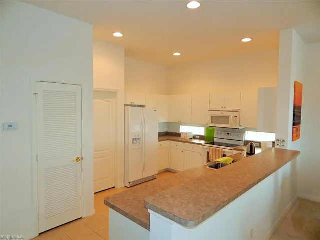 Kitchen with white appliances, a peninsula, recessed lighting, light tile patterned floors, and white cabinetry