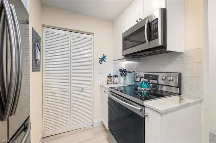 Kitchen with stainless steel appliances, white cabinetry, light countertops, and backsplash