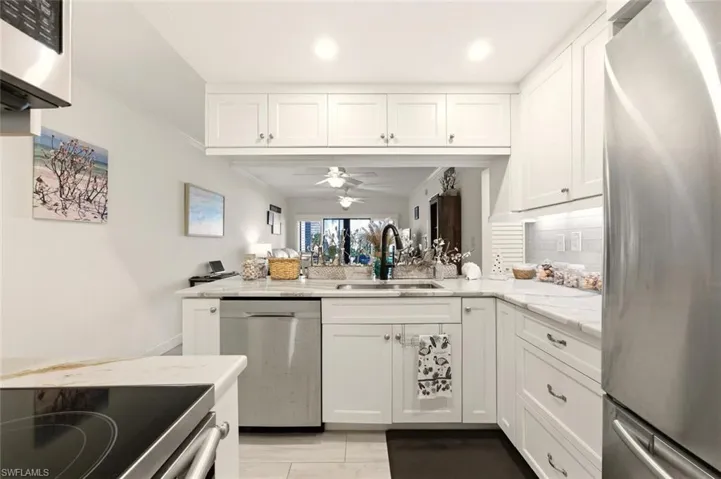 Kitchen with white cabinetry, stainless steel appliances, light stone countertops, ceiling fan, and ornamental molding