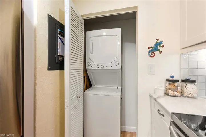 Laundry area featuring stacked washing machine and dryer, a textured wall, electric panel, and light wood-style flooring
