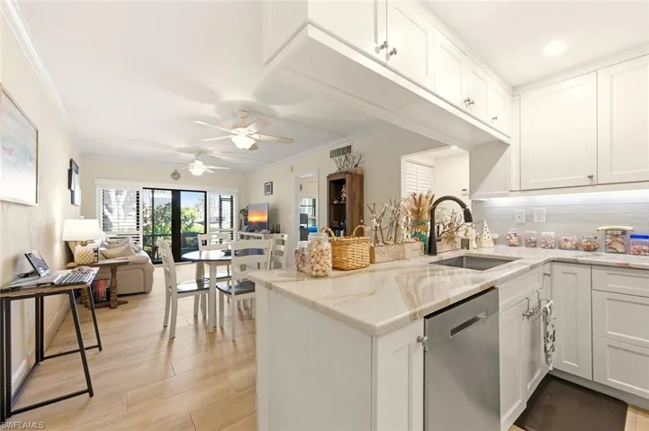Kitchen featuring white cabinetry, open floor plan, light stone counters, a ceiling fan, and ornamental molding