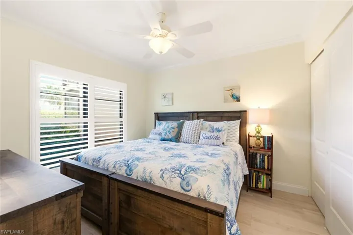 Bedroom with a closet, ornamental molding, light wood-style flooring, and a ceiling fan