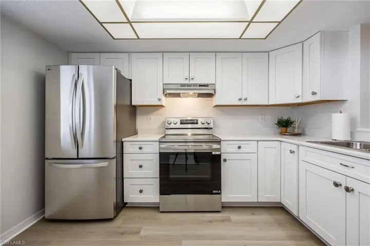 Kitchen with appliances with stainless steel finishes, white cabinets, light wood-style floors, under cabinet range hood, and light stone countertops