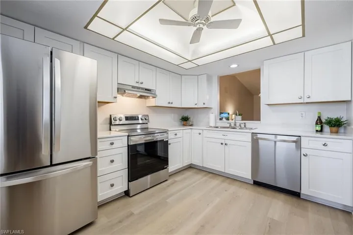 Kitchen featuring stainless steel appliances, white cabinets, under cabinet range hood, a ceiling fan, and light wood-type flooring