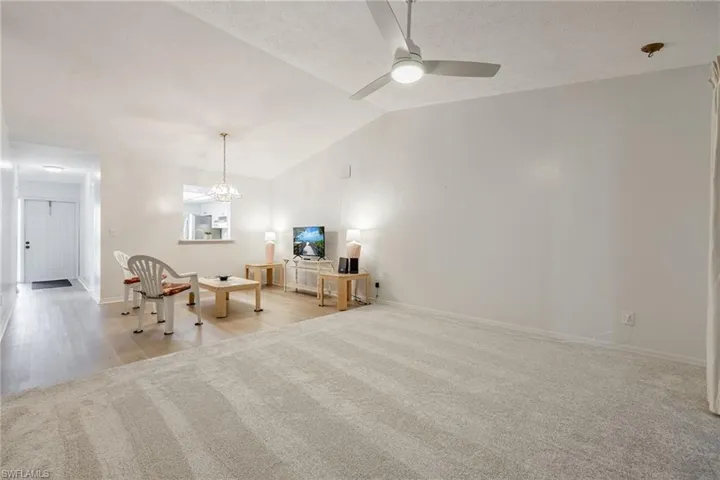 Living area featuring lofted ceiling, light carpet, a chandelier, and a ceiling fan and new carpet