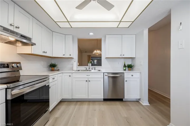 Kitchen with stainless steel appliances, white cabinets, under cabinet range hood, and light wood-style flooring
