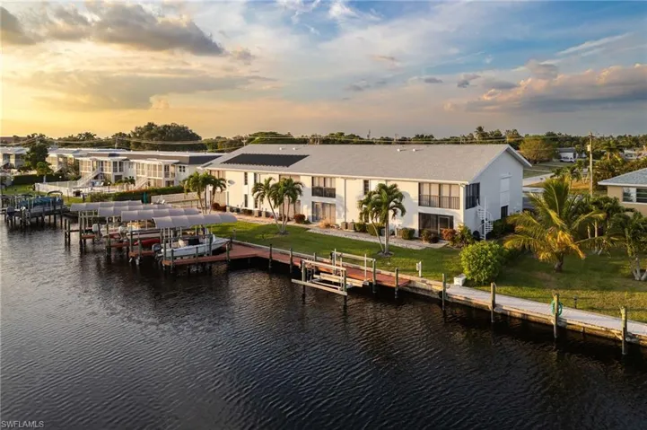 Back of property with boat lift, a water view, a yard, and stucco siding