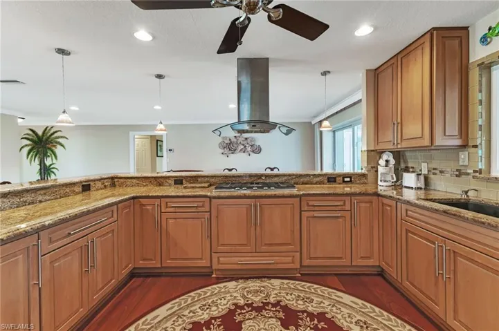 Kitchen featuring island exhaust hood, dark hardwood / wood-style flooring, ceiling fan, and light stone countertops