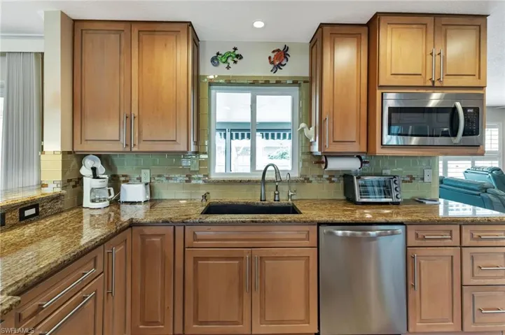 Kitchen with tasteful backsplash, appliances with stainless steel finishes, stone counters, and sink