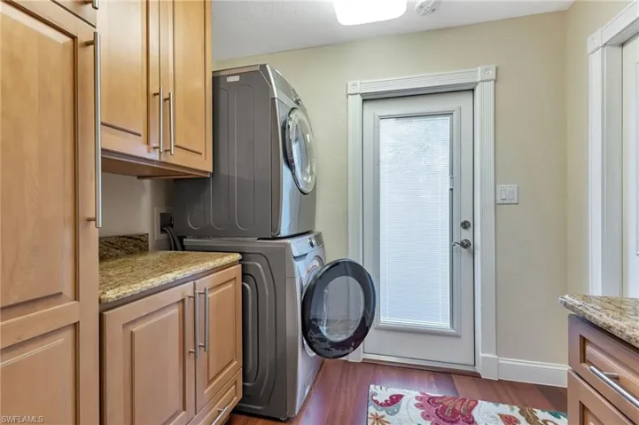 Clothes washing area featuring hardwood / wood-style flooring, stacked washer and dryer, and cabinets