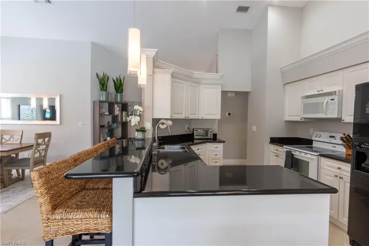 Kitchen featuring white appliances, light tile patterned flooring, pendant lighting, a peninsula, and a towering ceiling