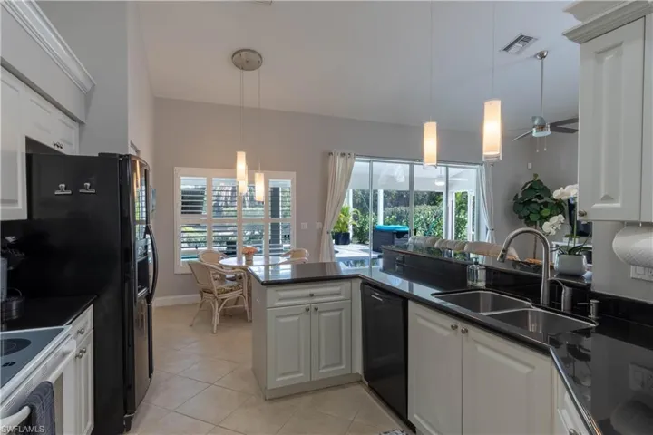 Kitchen with hanging light fixtures, white cabinetry, light tile patterned floors, black dishwasher, and a peninsula