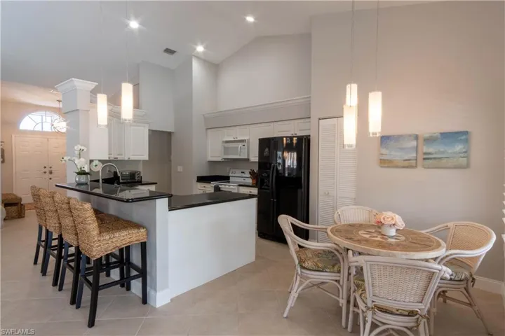 Kitchen with white appliances, high vaulted ceiling, white cabinets, a peninsula, and a breakfast bar