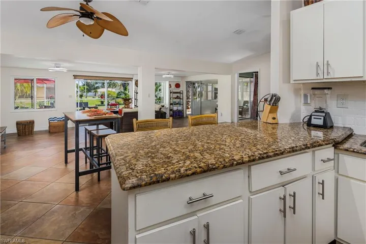Kitchen featuring decorative backsplash, dark tile patterned floors, ceiling fan, dark stone countertops, and white cabinetry
