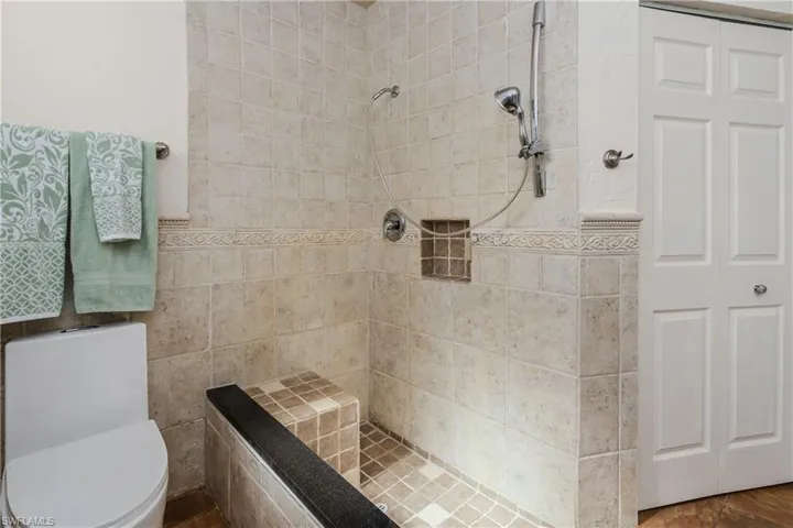 Bathroom featuring toilet, tiled shower, and tile walls