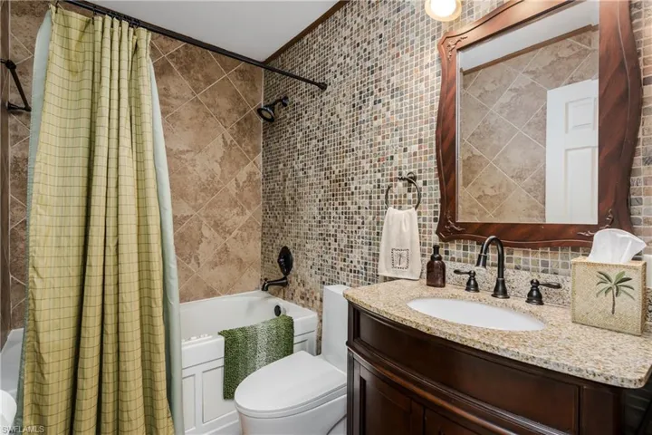 Full bathroom featuring vanity, decorative backsplash, toilet, tile walls, and shower / tub combo