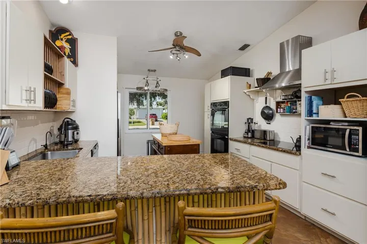 Kitchen featuring sink, a kitchen bar, decorative backsplash, white cabinets, and black appliances