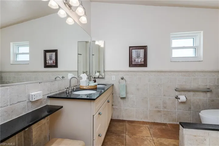 Bathroom with vanity, tile patterned floors, tile walls, and lofted ceiling