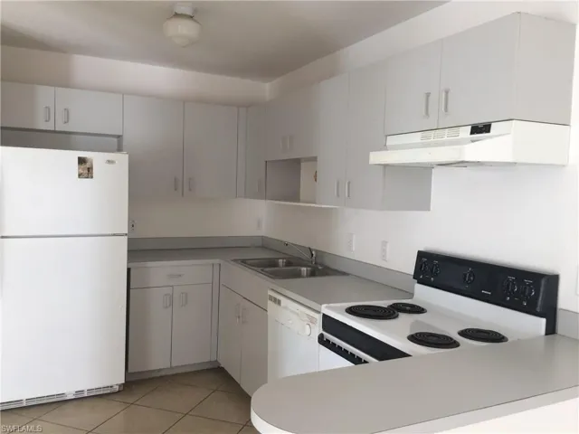 Kitchen with white appliances, light tile patterned floors, light countertops, a peninsula, and white cabinets