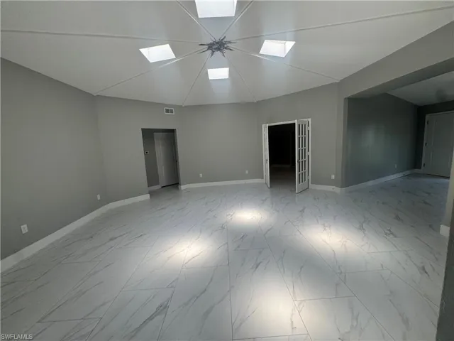 Spacious room featuring a vaulted ceiling with skylights, light gray walls, and large format marble-look tile flooring with sun light