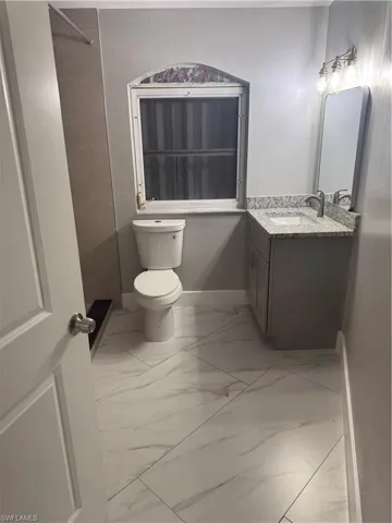 The bathroom features a vanity with a granite countertop, a mirror, and a window with an arched decorative element