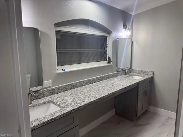 Bathroom featuring a dual sink vanity with granite countertops, light grey cabinetry, and tiled flooring