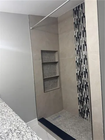 The shower stall features neutral-toned wall tiles, a decorative mosaic tile accent strip, and a built-in recessed shelf