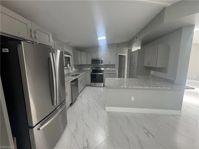 The kitchen features stainless steel appliances, grey cabinetry, light-colored granite countertops, and a breakfast bar