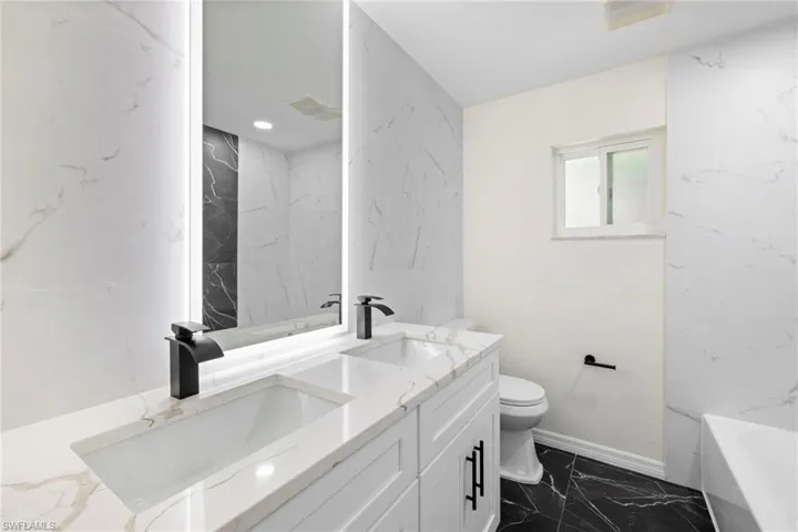 Bathroom featuring double vanity, marble finish flooring, a tub, stone wall, and recessed lighting